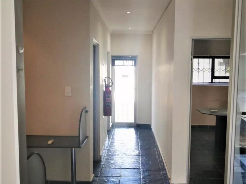 A functional commercial hallway featuring dark tiled flooring, recessed lighting, and a built-in counter, leading to an exterior security door.