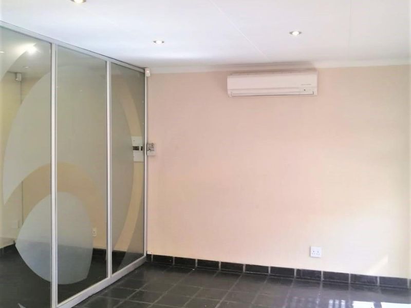 A clean, vacant office space featuring dark tiled flooring, a glass partition wall, and a wall-mounted air conditioning unit.