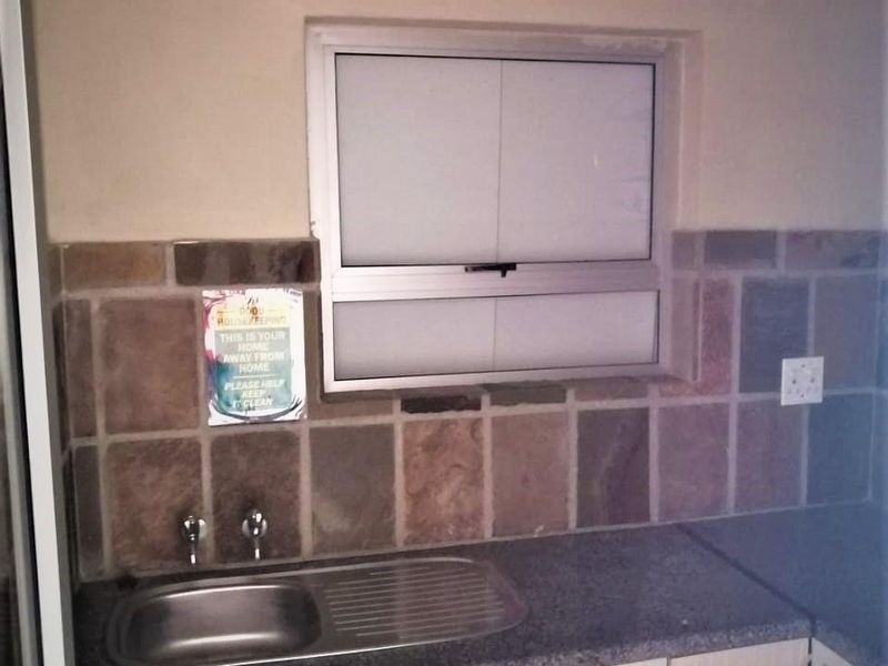 A functional kitchen area featuring a stainless steel sink, stone tile backsplash, laminate countertops, and built-in cabinetry with an aluminum window.