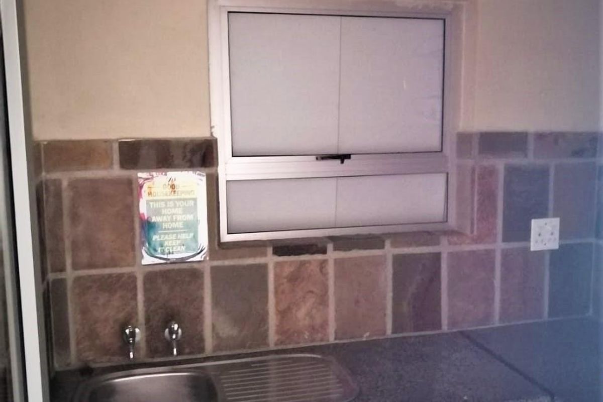 A functional kitchen area featuring a stainless steel sink, stone tile backsplash, laminate countertops, and built-in cabinetry with an aluminum window.