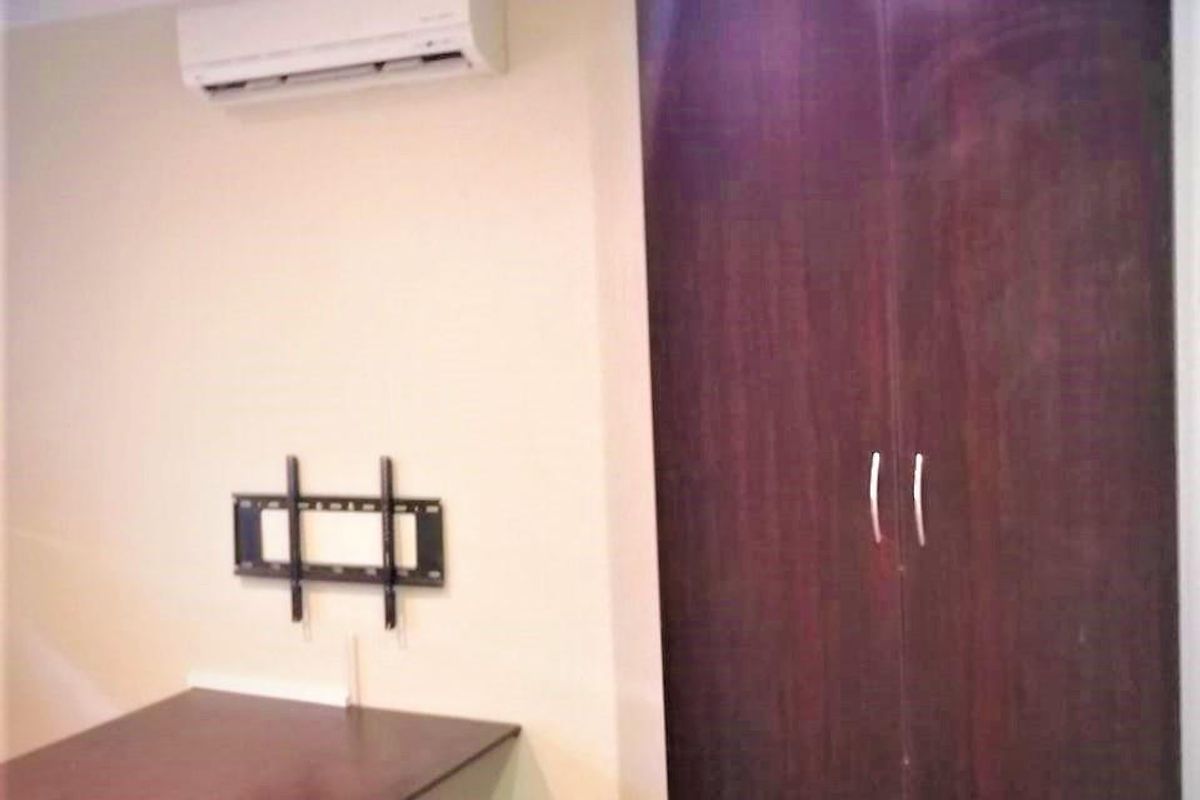 A functional bedroom space featuring a built-in dark wood wardrobe, wall-mounted air conditioning unit, and a fixed desk surface.