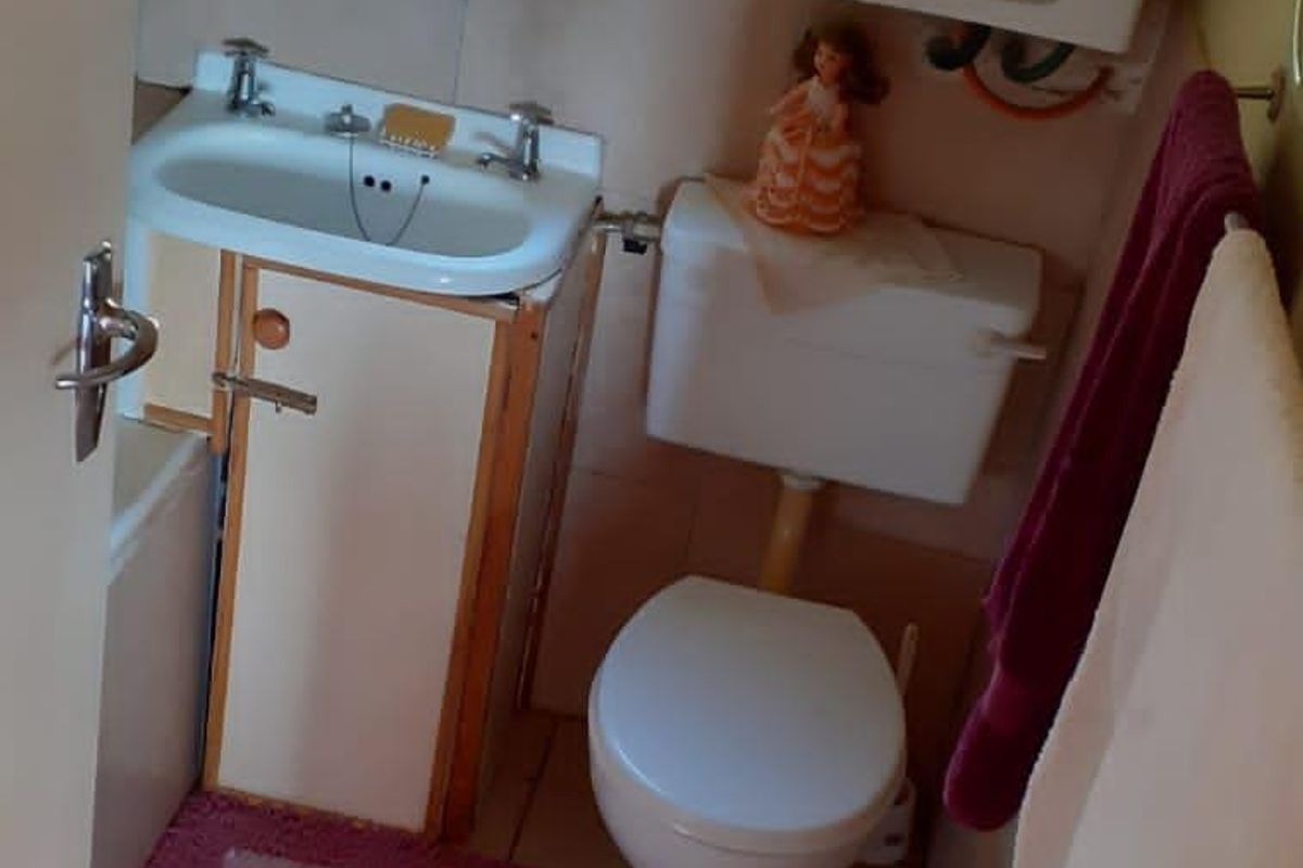 Compact bathroom featuring a wall-mounted boiler, pedestal basin with vanity cabinet, and standard toilet suite with tiled flooring.