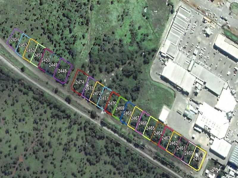 Aerial view of a series of residential land parcels with marked boundaries, situated in a vegetated area near commercial infrastructure.
