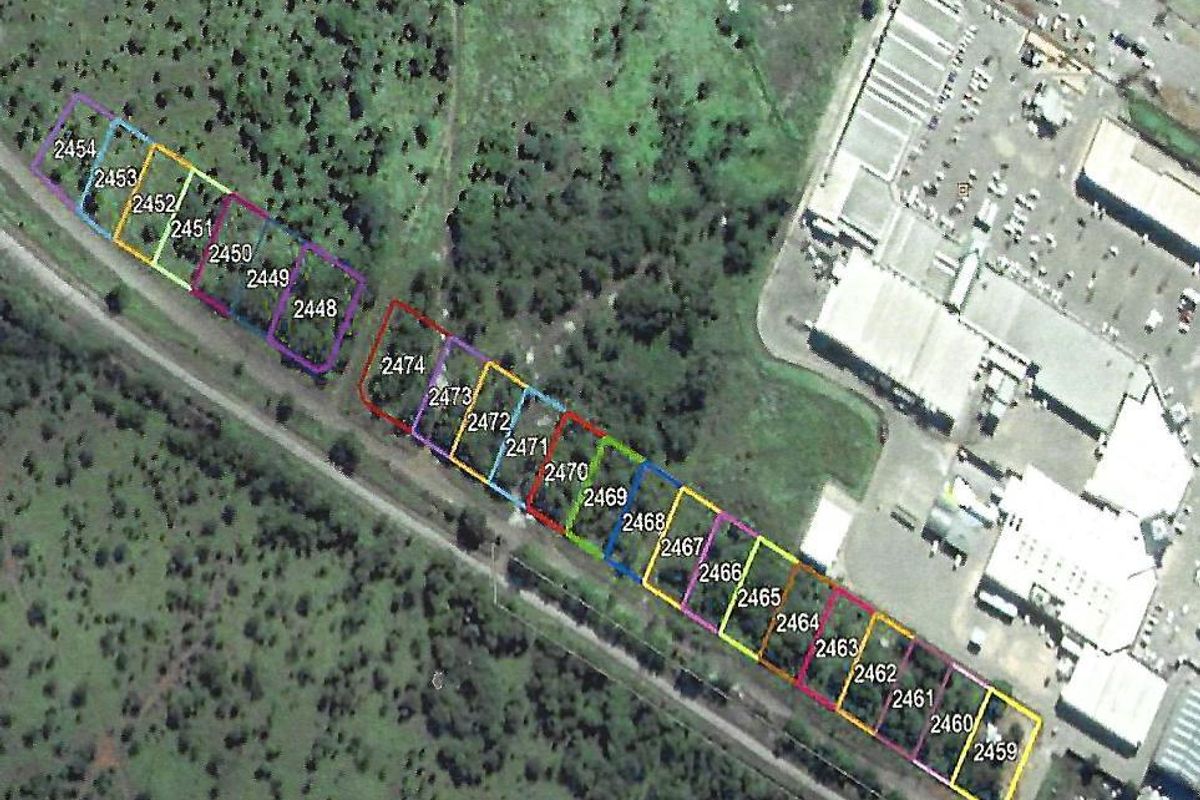 Aerial view of a series of residential land parcels with marked boundaries, situated in a vegetated area near commercial infrastructure.