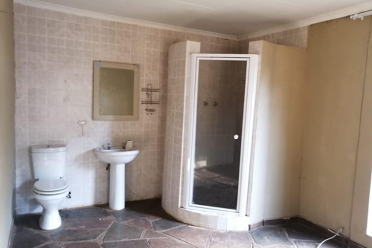A dated bathroom featuring a pedestal basin, toilet, and a corner shower enclosure with stone flooring and tiled wall finishes.