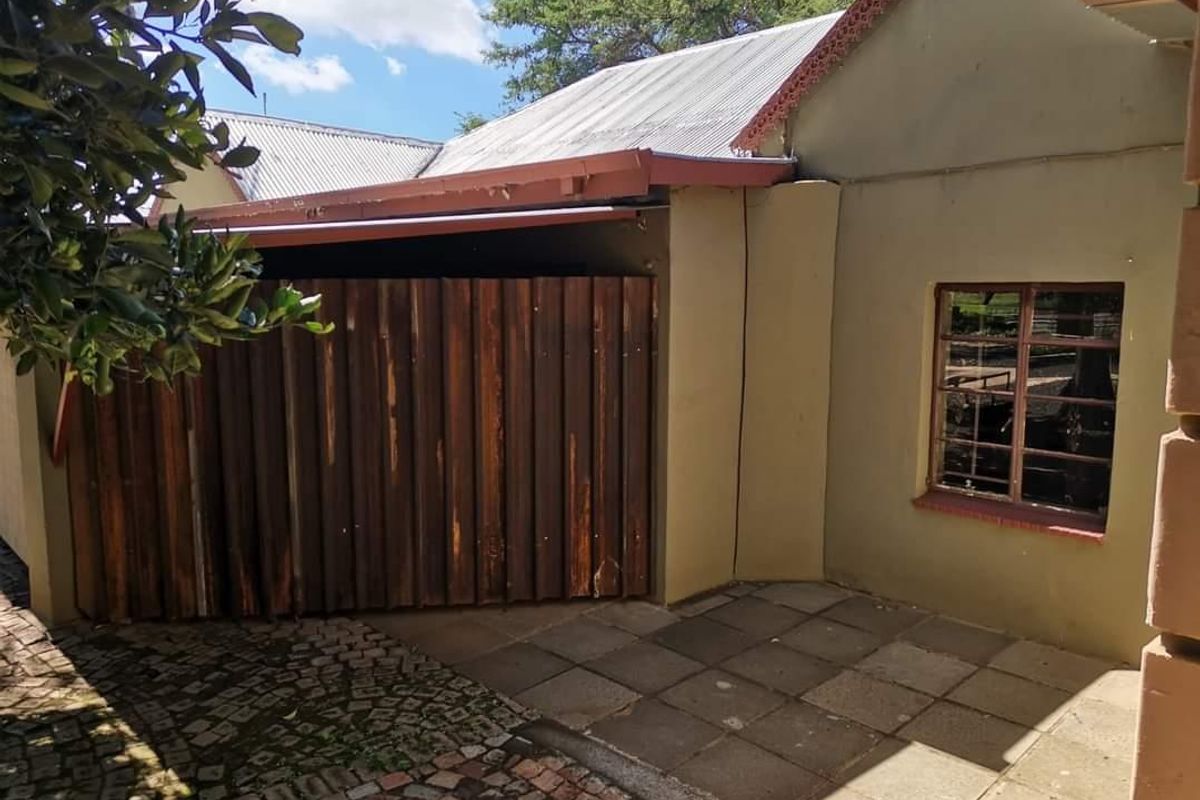 Rear exterior view of the farm property featuring a paved patio area, corrugated iron roofing, and a timber gate entrance.