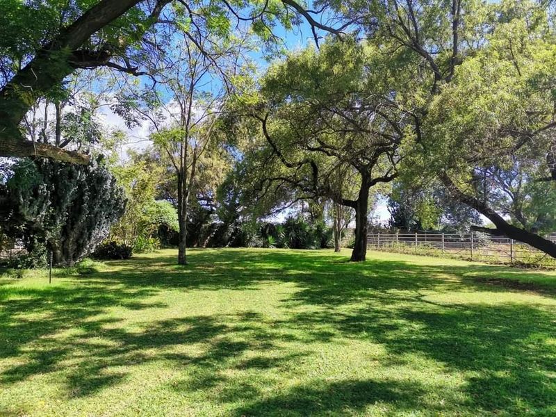 A spacious, well-maintained garden area featuring mature trees, expansive lawn, and perimeter wire fencing on the farm property.