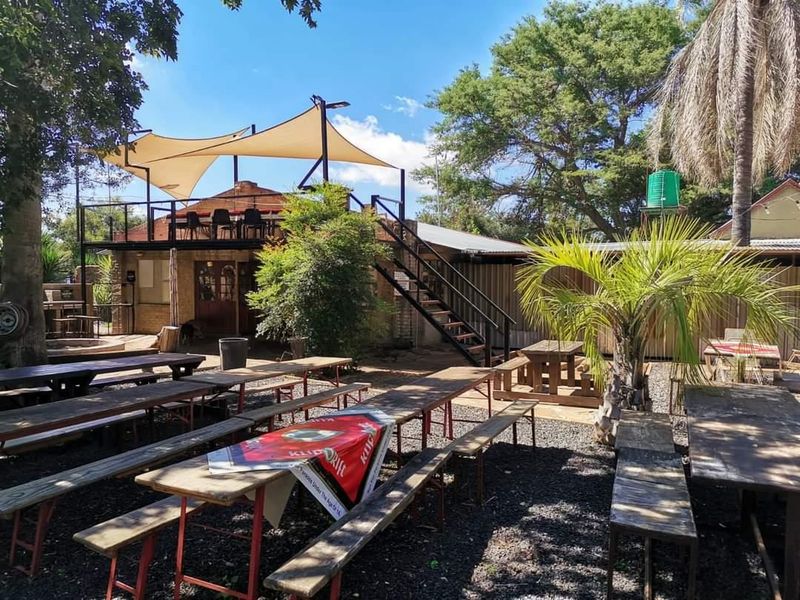 Outdoor entertainment area featuring a raised deck with shade sail, metal staircase access, and gravel seating area, suitable for farm-style hospitality or events.