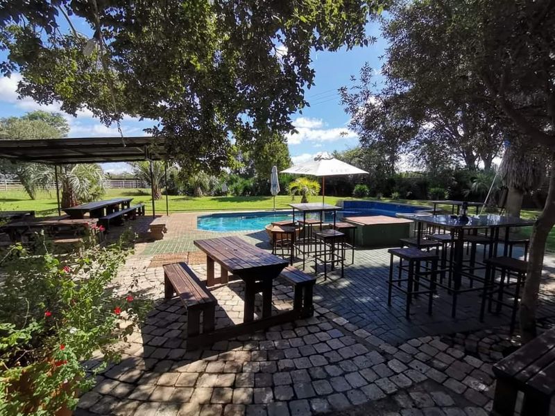 Outdoor entertainment area featuring a swimming pool, paved patio space, and a covered seating area set within a spacious garden environment.