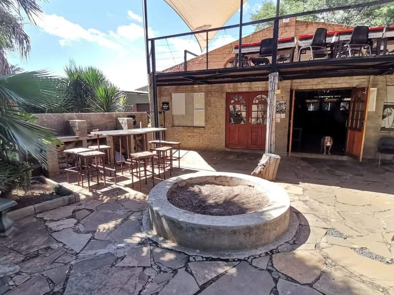 Outdoor entertainment area featuring a stone-paved patio, built-in braai, central fire pit, and a raised deck with metal structure.
