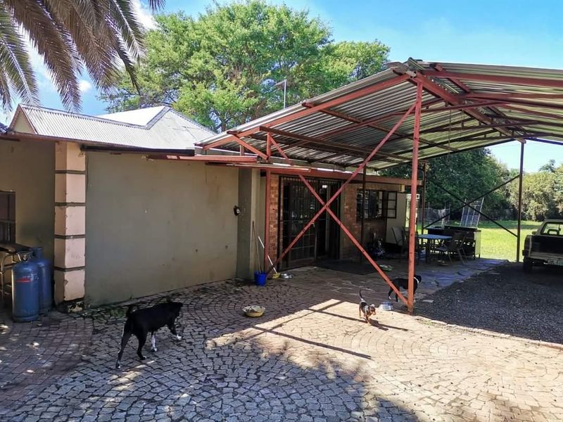 A covered outdoor patio area featuring a corrugated metal roof, steel support structure, and cobblestone paving, providing a functional space for outdoor living.