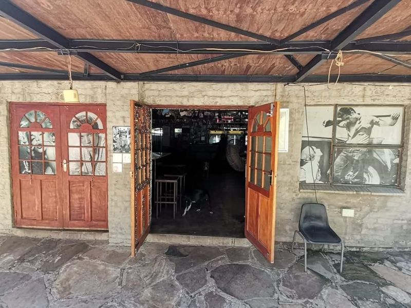 Covered patio area featuring stone flooring, exposed timber ceiling, and double wooden entrance doors leading into the main building.