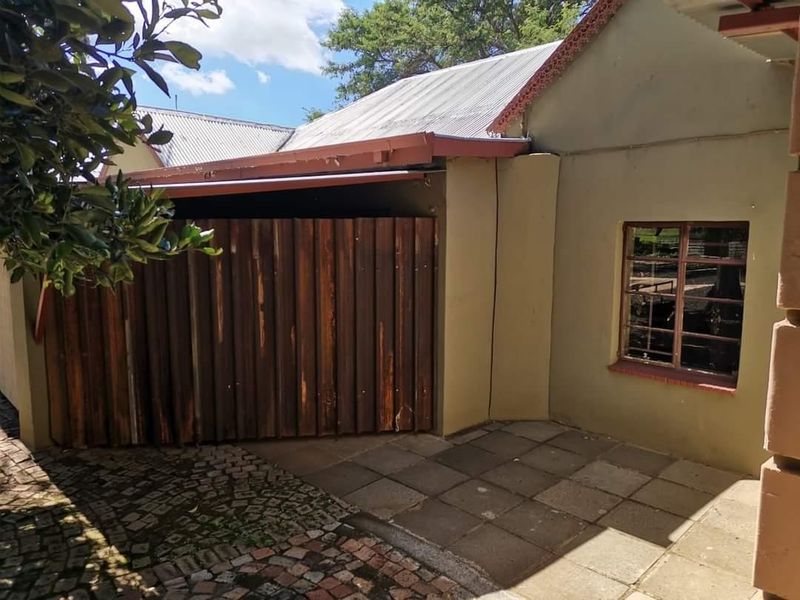 Rear exterior view of the farm property featuring a paved patio area, corrugated iron roofing, and a timber gate entrance.