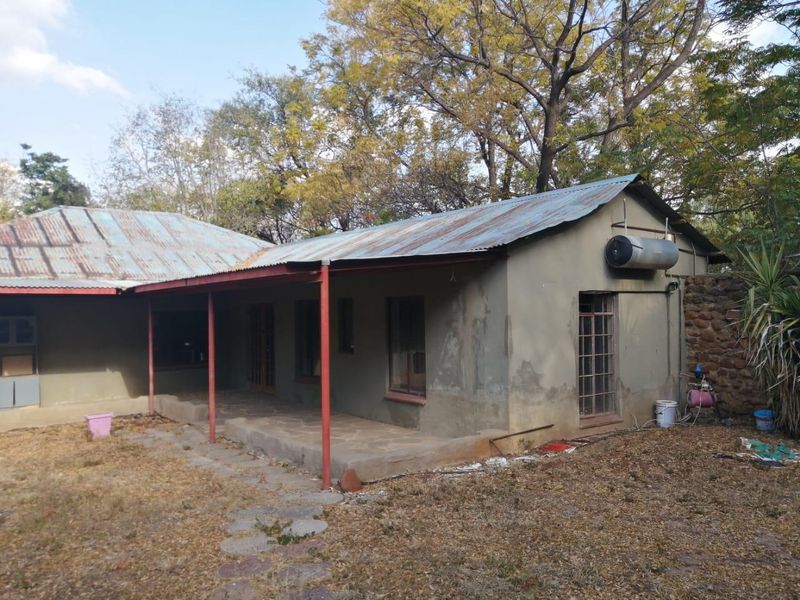 Rear view of a farm dwelling featuring a covered patio, corrugated metal roofing, and an external solar geyser unit.