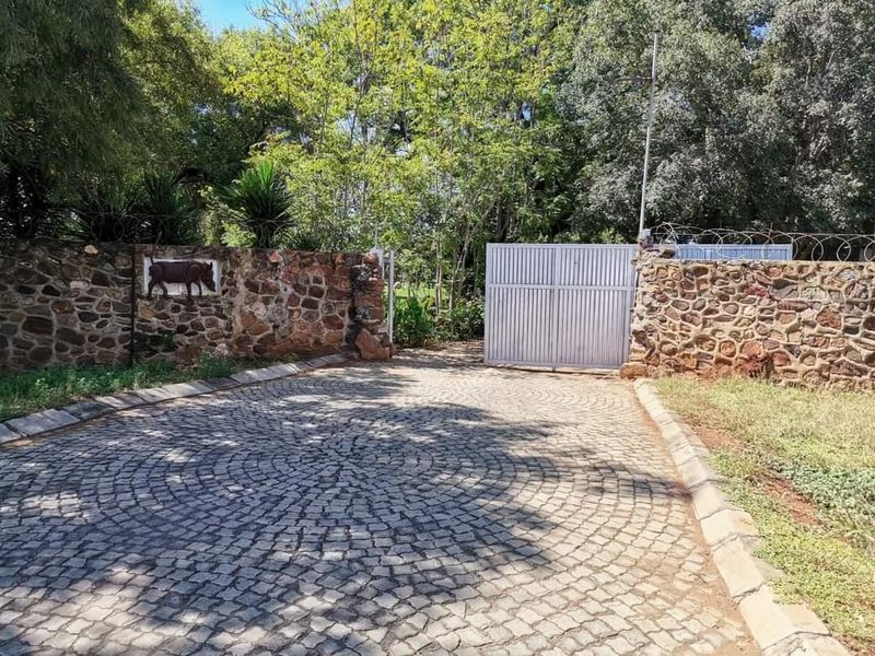 Front entrance of the farm property featuring a cobblestone driveway, stone boundary walls, and a secure metal gate.