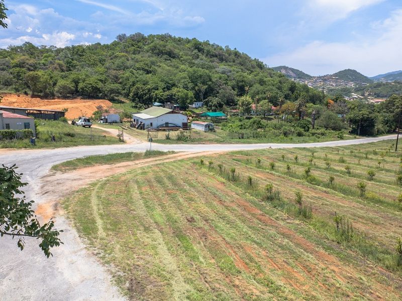 An aerial view of a farm property featuring open land, an orchard, and various outbuildings set against a hilly landscape.
