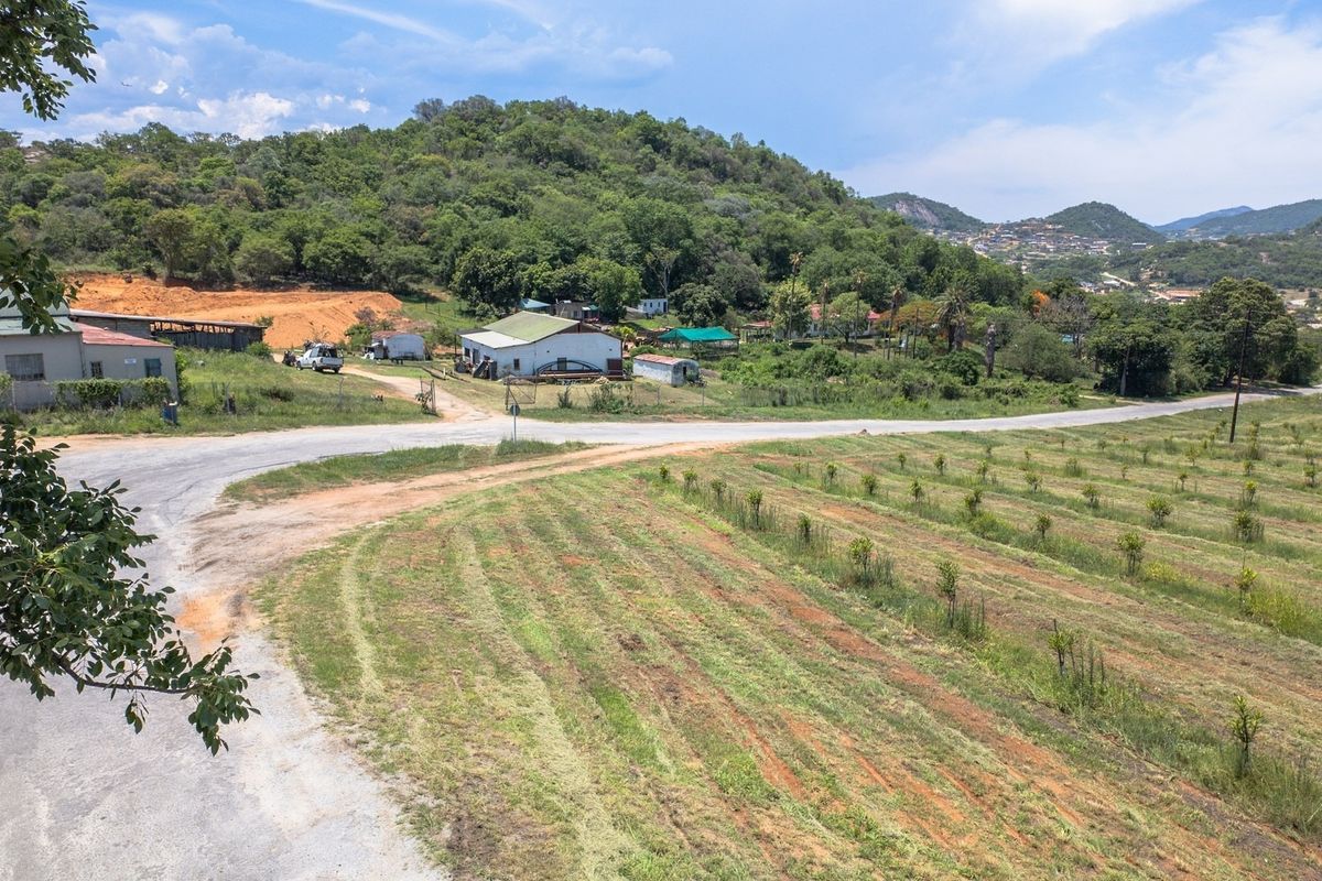 An aerial view of a farm property featuring open land, an orchard, and various outbuildings set against a hilly landscape.