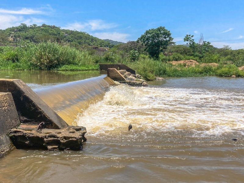 A view of a concrete weir structure spanning a river on the farm property, showing natural water flow and surrounding landscape.