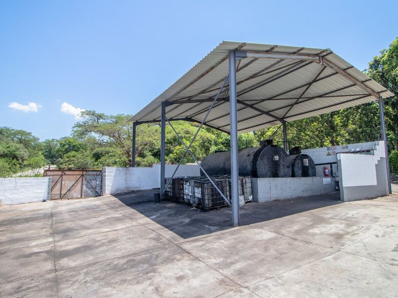 A functional outdoor utility area featuring a covered metal structure, concrete flooring, and industrial fuel storage tanks on a farm property.