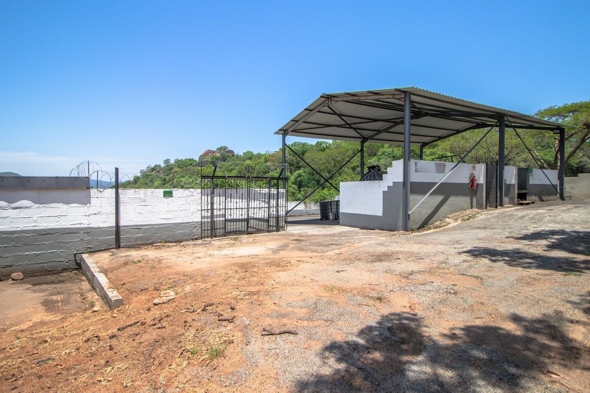 An outdoor utility area featuring a covered metal structure, perimeter wall with security fencing, and a concrete driveway on a farm property.