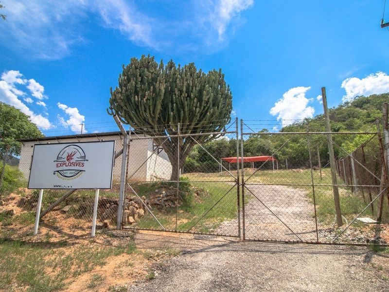 Front entrance view of the property featuring a gated gravel driveway, chain-link perimeter fencing, and established landscaping.