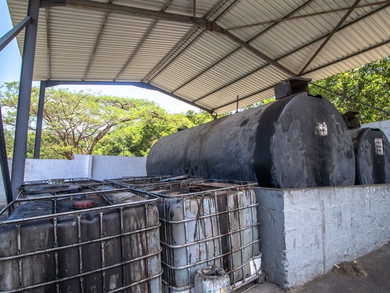 Industrial utility area featuring a covered structure with large fuel storage tanks and IBC containers within a concrete containment wall.