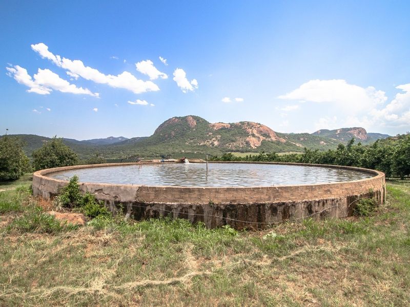 A large circular concrete water reservoir situated on the farm, featuring mountain views and surrounding orchard trees.