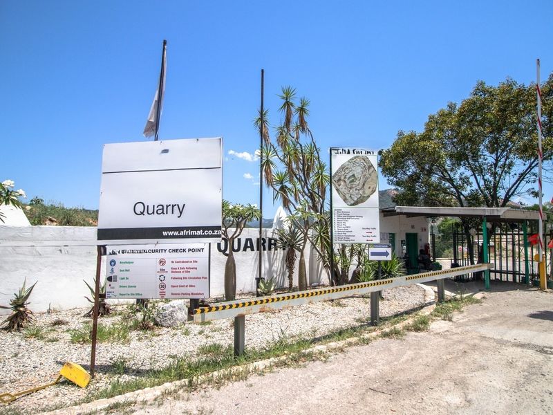 The entrance to the quarry site featuring a security checkpoint, boom gate, and perimeter wall with site signage.