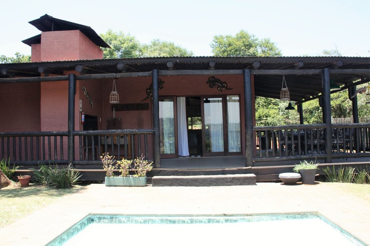 Rear exterior view featuring a covered timber patio, built-in fireplace, and a swimming pool set in a landscaped garden area.
