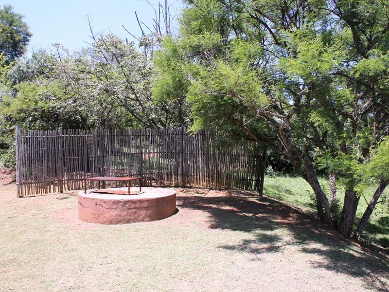 A garden area featuring a circular brick masonry structure and natural bamboo fencing surrounded by mature trees.