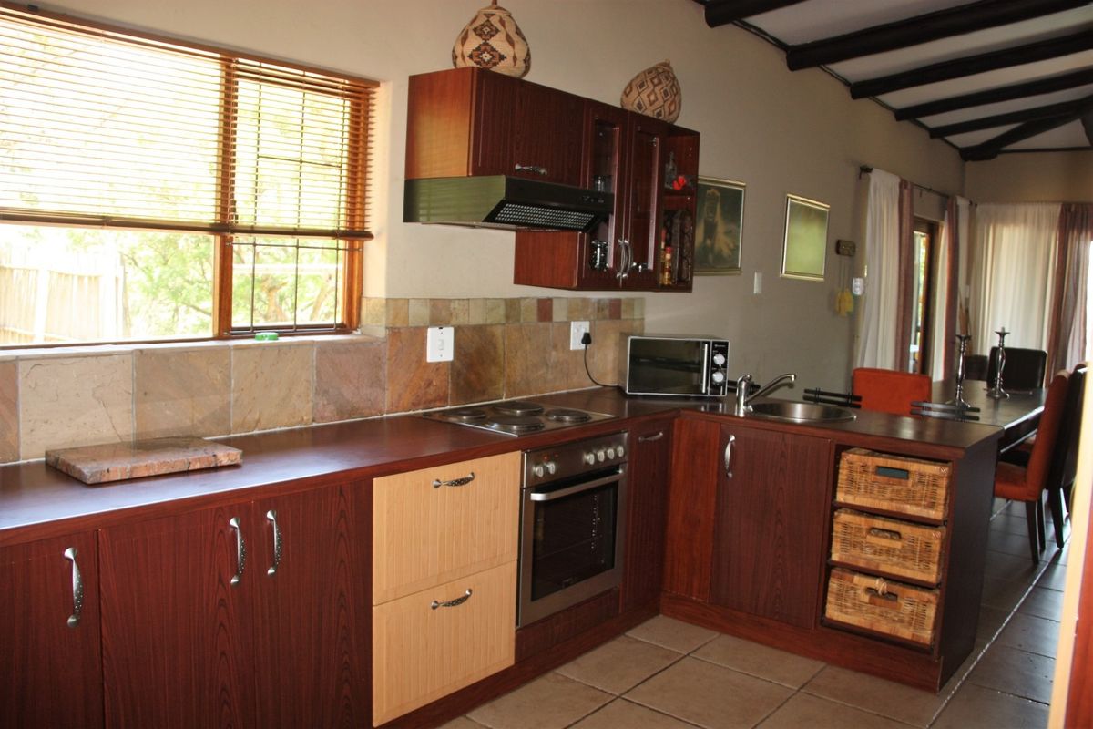 A functional kitchen featuring dark wood cabinetry, laminate countertops, built-in oven and hob, tiled backsplash, and exposed timber ceiling beams.