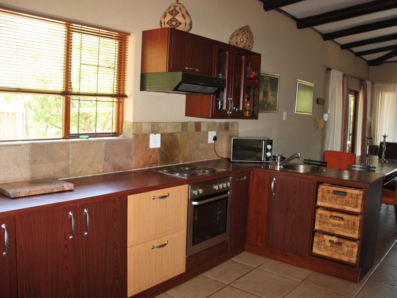 A functional kitchen featuring dark wood cabinetry, laminate countertops, built-in oven and hob, tiled backsplash, and exposed timber ceiling beams.