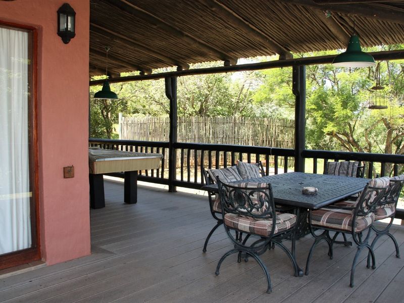 A spacious covered patio featuring timber decking, a rustic thatched roof, and timber balustrades, offering an ideal outdoor entertainment area overlooking the garden.