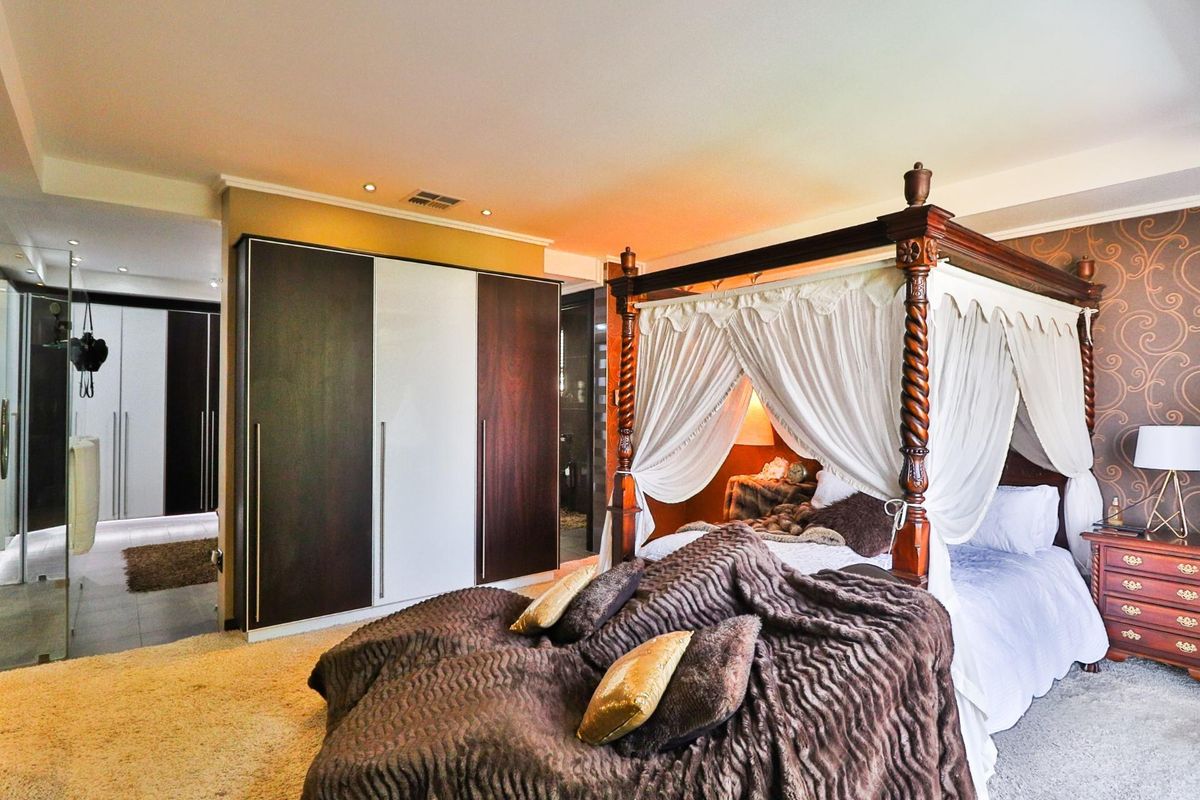 Spacious bedroom featuring built-in floor-to-ceiling wardrobes and recessed ceiling lighting, with an adjoining en-suite bathroom visible in the background.