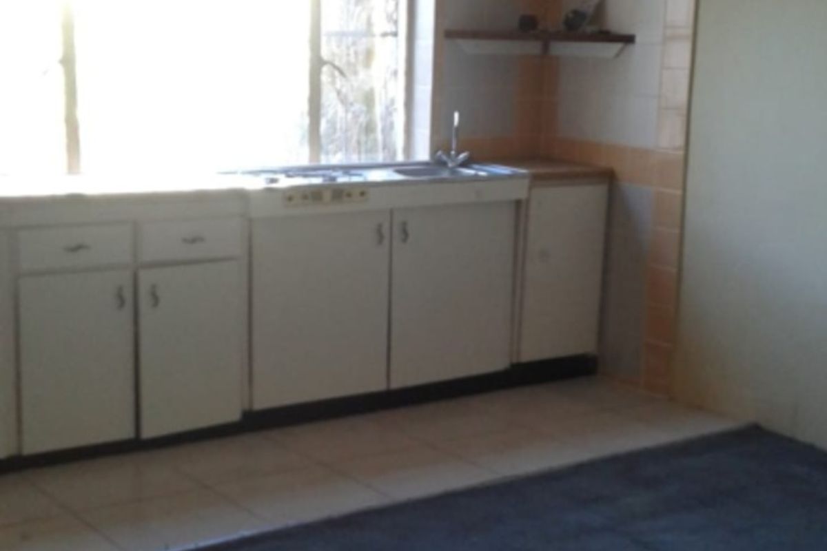 A dated kitchen area featuring original cabinetry, tiled splashbacks, and an exposed timber ceiling grid, offering significant potential for modernization and renovation.