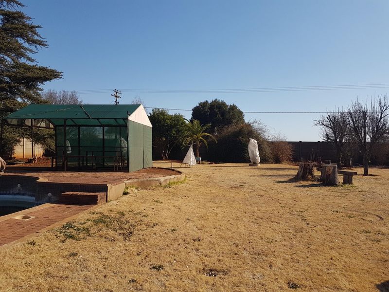 Outdoor pool area featuring a brick surround and a large shade cloth structure set within a dry garden space.