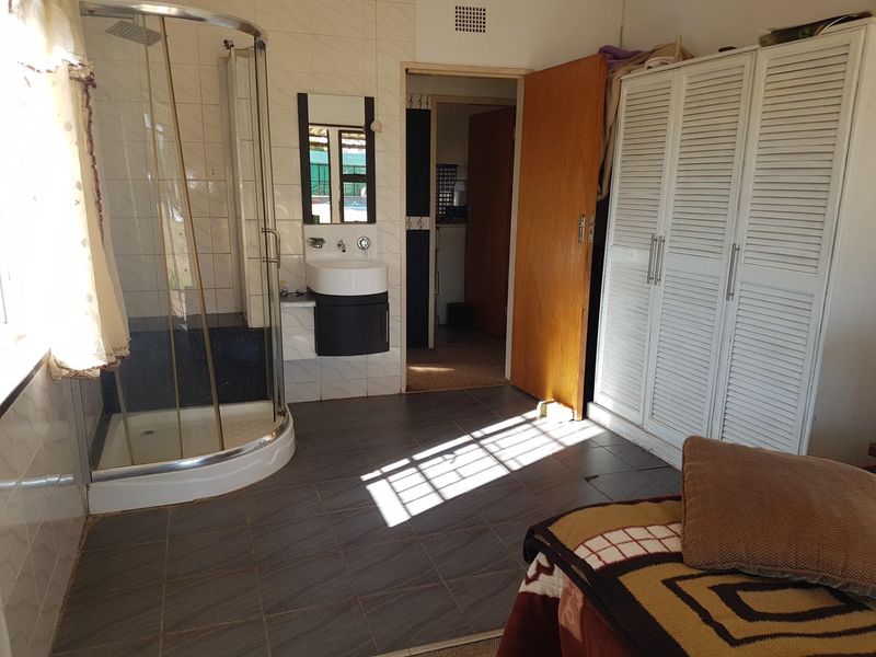 A functional bathroom featuring a corner shower, wall-mounted vanity basin, and integrated louvered wardrobe storage, finished with tiled surfaces.