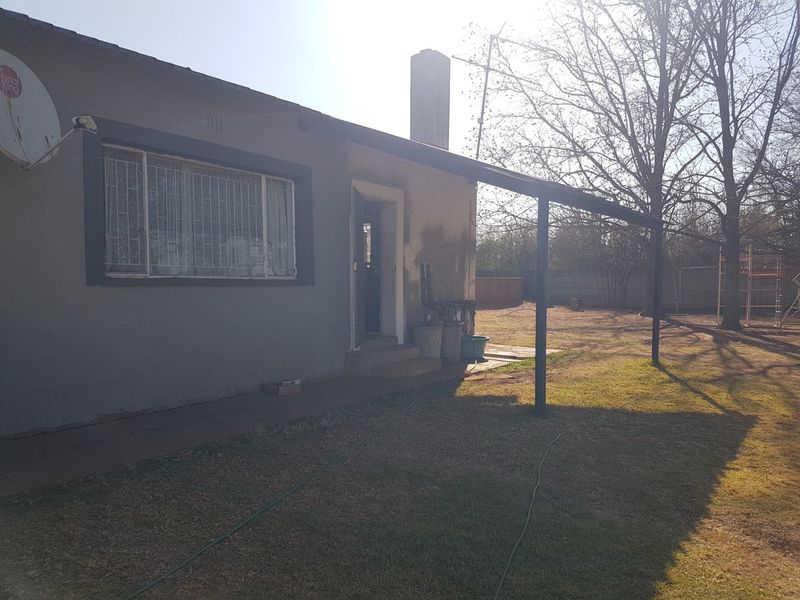 Rear exterior view of the property featuring a patio structure, chimney, and security bars on windows, set within a large garden area.