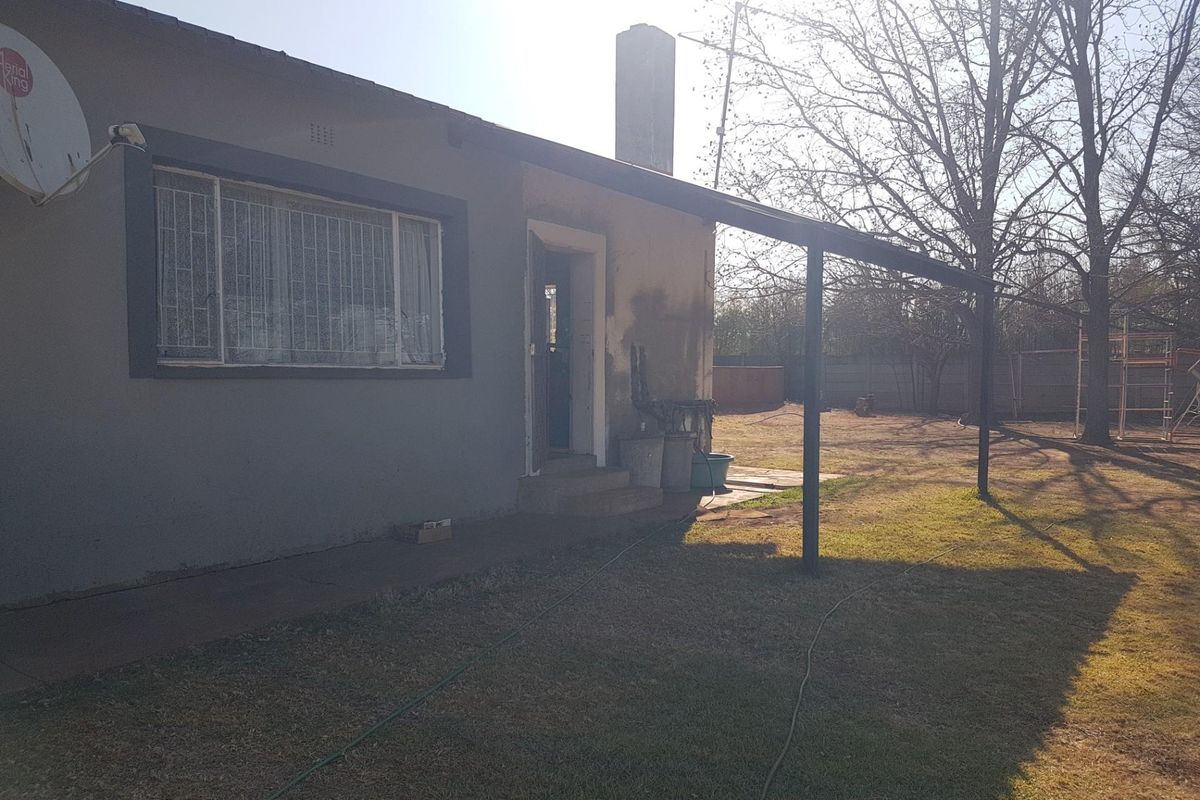 Rear exterior view of the property featuring a patio structure, chimney, and security bars on windows, set within a large garden area.