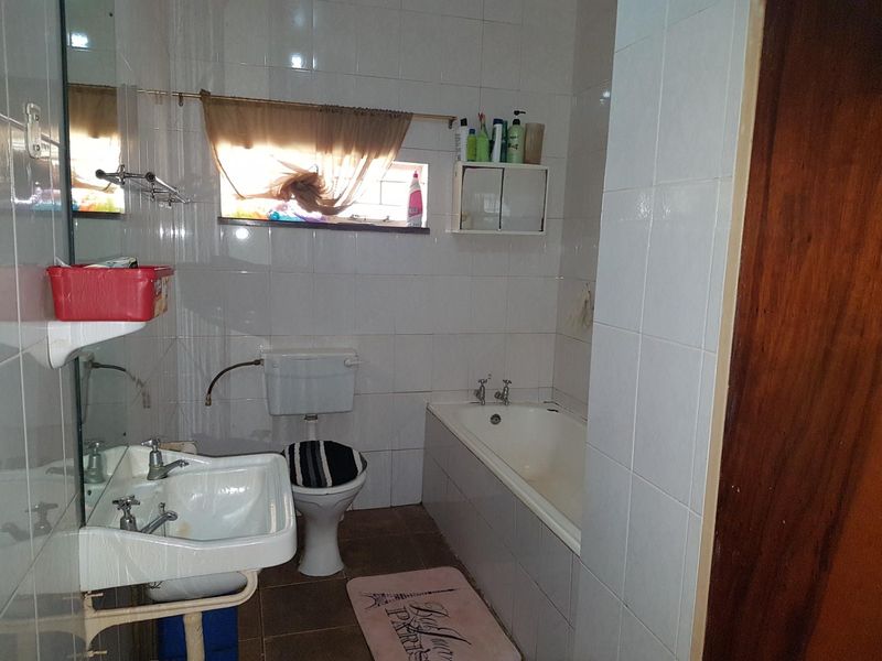 A functional bathroom featuring a built-in bathtub, wall-mounted basin, and toilet with high-level cistern, finished with full-height wall tiling.