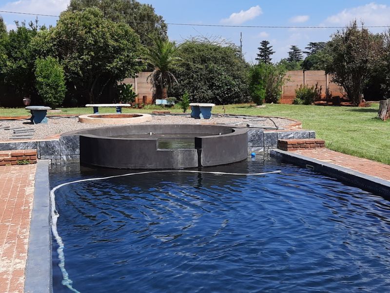 Outdoor pool area featuring a raised circular water feature, brick paving, and gravel landscaping set within a spacious garden with boundary walling.