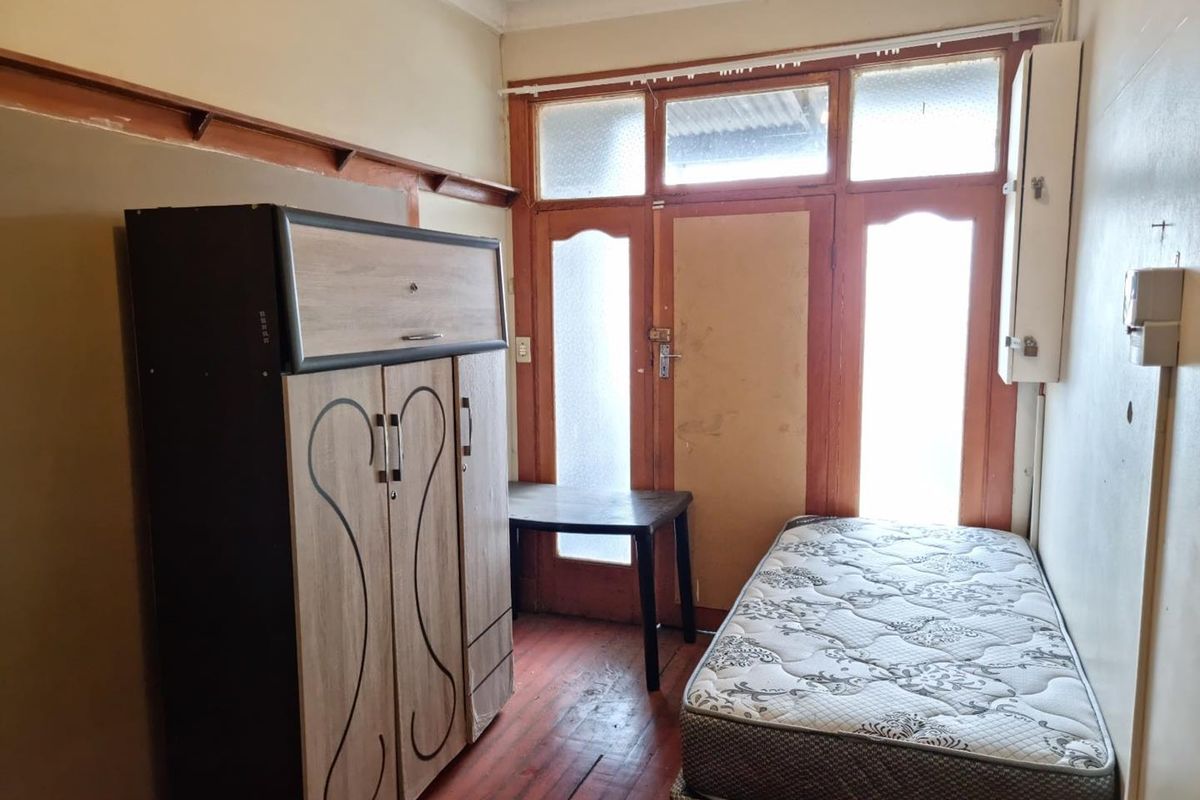 A compact bedroom featuring original timber flooring, decorative ceiling cornice, and direct access to an exterior area through a multi-pane glass door.