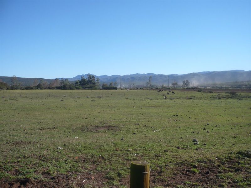 Expansive open farmland view featuring wire fencing and distant mountain ranges under a clear blue sky.