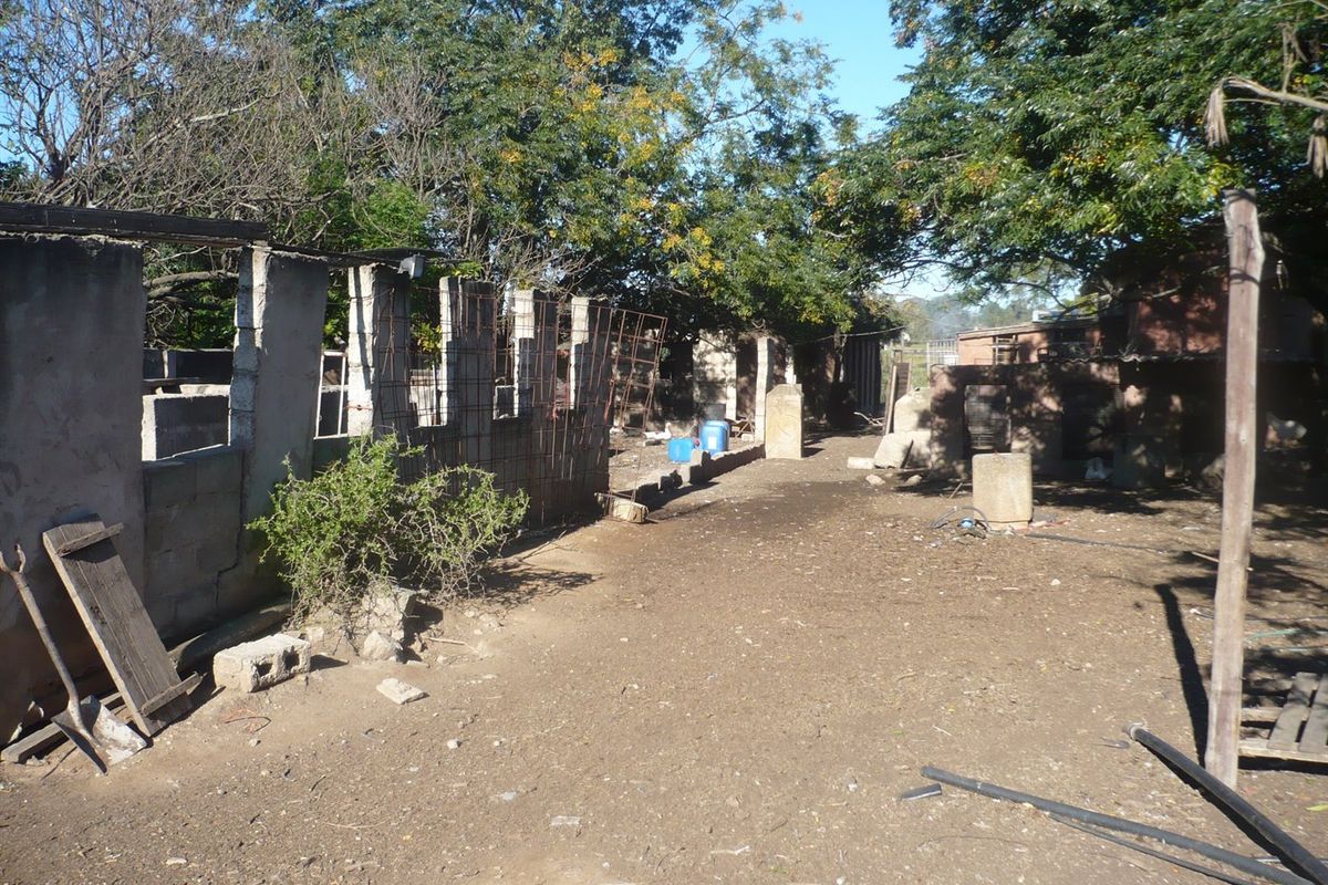 Rear exterior view of a farm property showing incomplete concrete block structures and exposed framing in a rural setting.