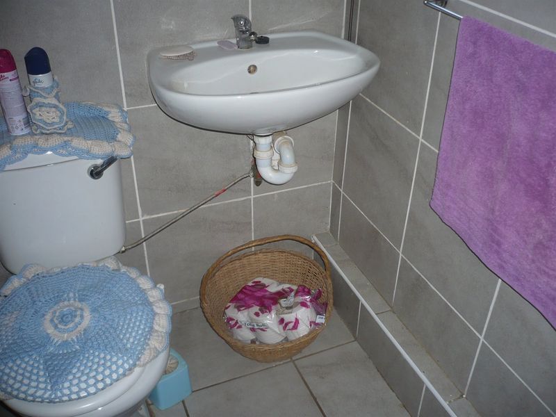 A functional bathroom featuring a wall-mounted basin, toilet, and neutral grey wall and floor tiling.