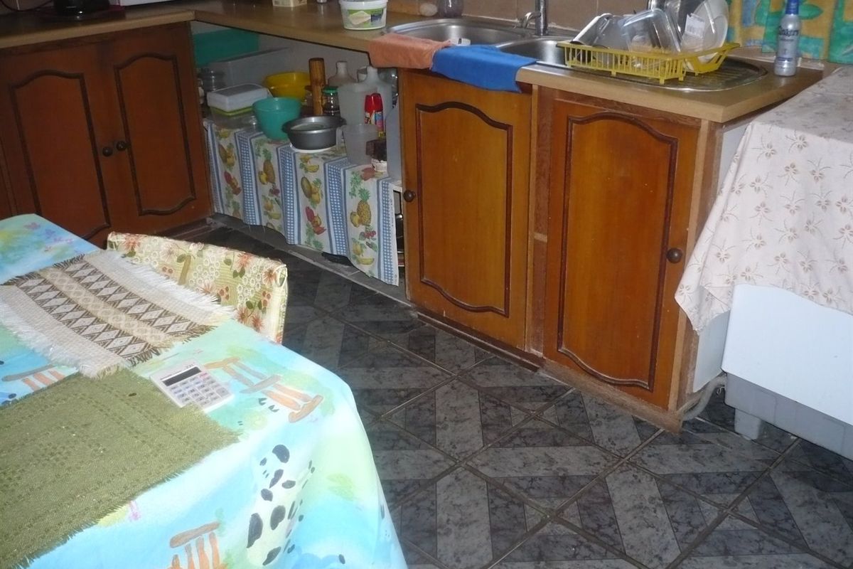 A dated kitchen area featuring traditional wooden cabinetry, a double basin sink, and patterned tiled flooring, offering potential for a modern renovation.