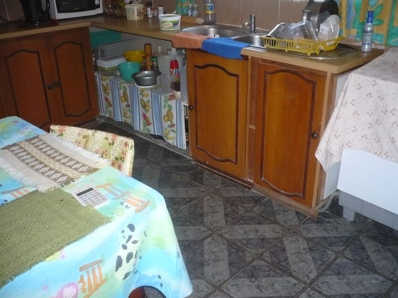 A dated kitchen area featuring traditional wooden cabinetry, a double basin sink, and patterned tiled flooring, offering potential for a modern renovation.