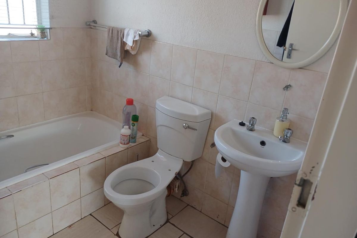 A functional bathroom featuring a bathtub, pedestal basin, and toilet with neutral wall and floor tiling, offering potential for modernization.