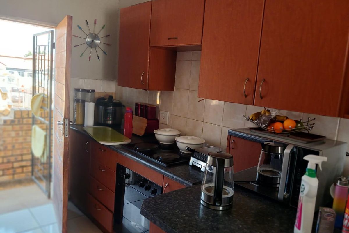 Compact kitchen featuring wood-look cabinetry, dark laminate countertops, built-in oven, electric hob, and tiled backsplash with direct access to an exterior security gate.