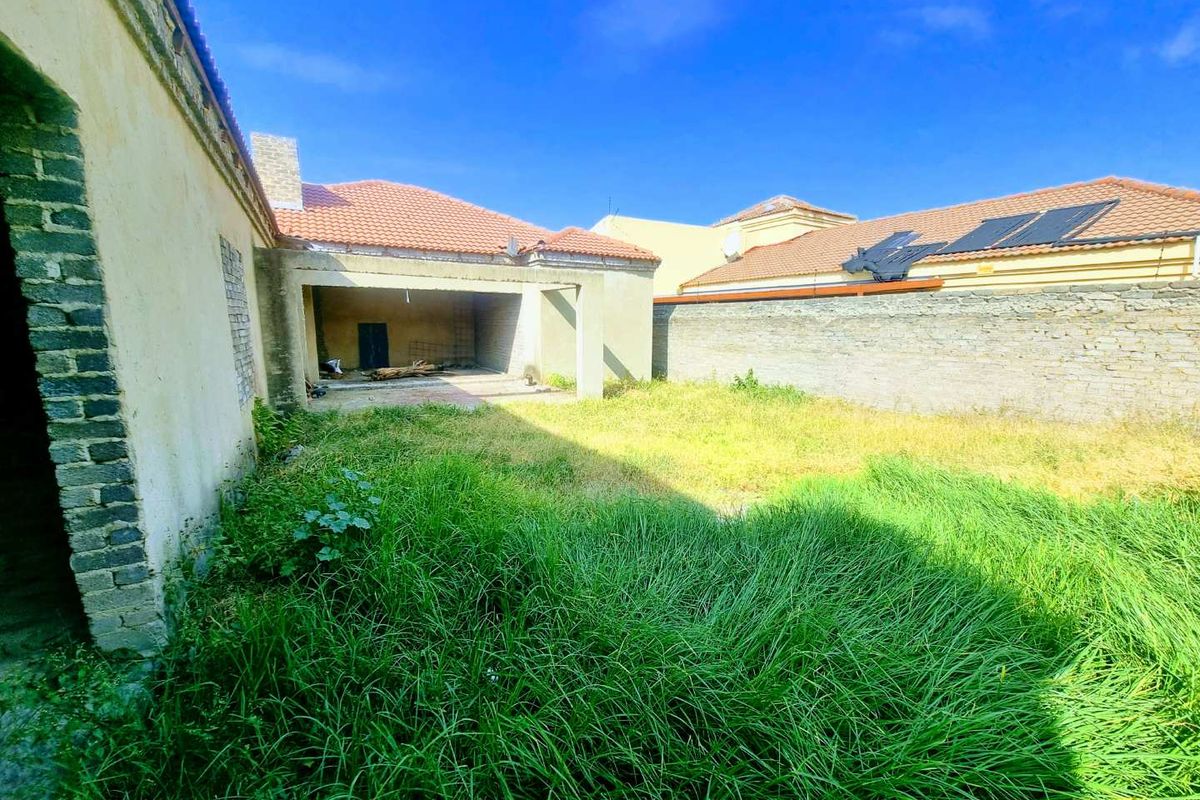 Rear view of the property featuring an overgrown garden area and a covered patio space requiring completion and landscaping.